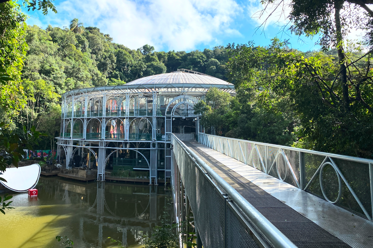 An auditorium in the middle of the trees with a bridge over a lake.