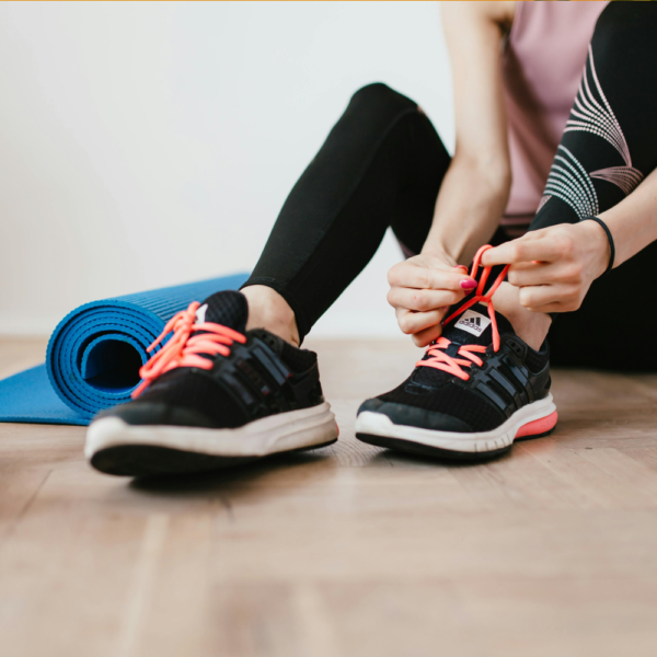 A woman sitting on the floor, tying her shoelaces, with a purple weight and a blue mat beside her.