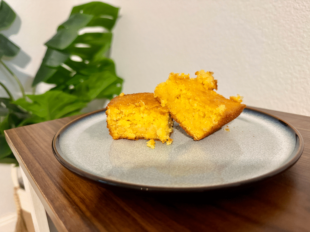 Piece of corn cake on a ceramic plate, with a plant in the background.
