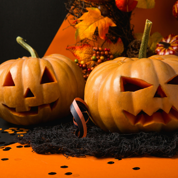Two Halloween pumpkins surrounded by festive confetti and streamers in classic orange, black, and purple colors, creating a playful and celebratory atmosphere.