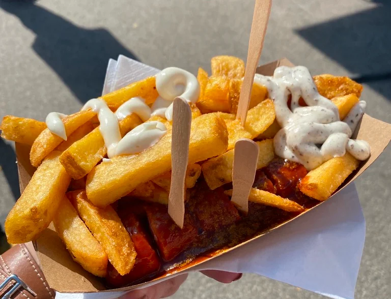 Traditional Berlin currywurst with fries served on a paper tray.