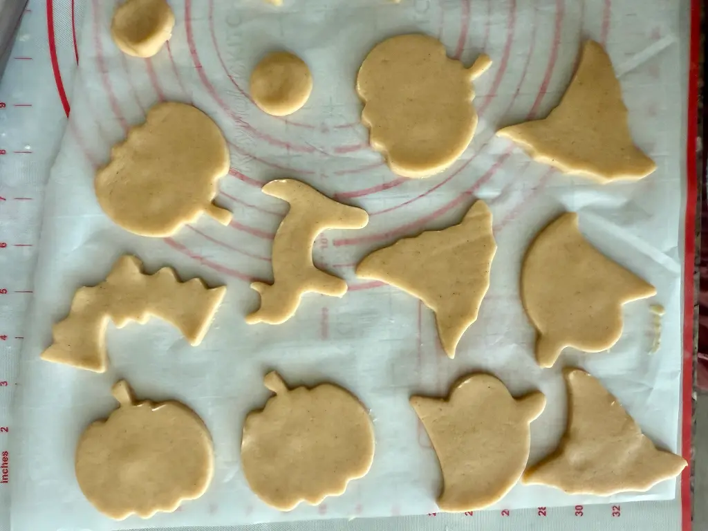 Shape the Halloween cookies using cutters such as ghost, pumpkin, bat, witch hat, and cat designs.